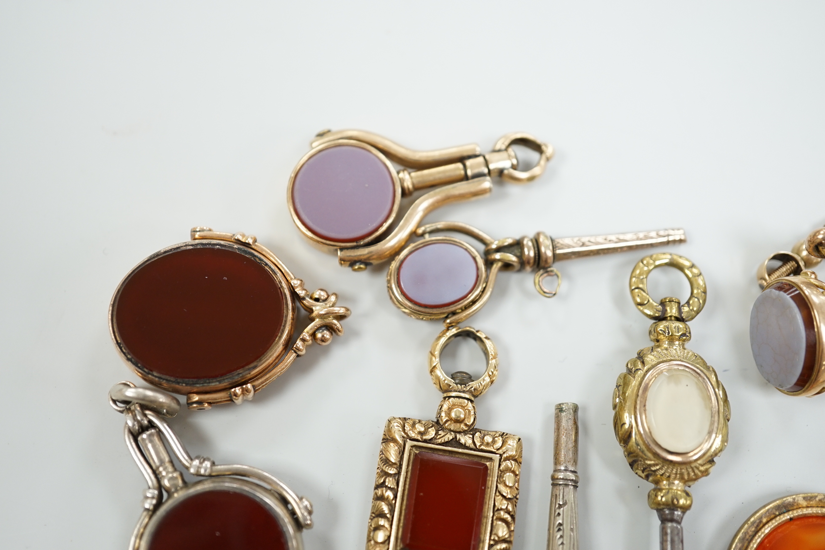 Sixteen assorted 19th century and later, 9ct gold and yellow or white metal overlaid and chalcedony set watch keys, including bloodstone, sardonyx, banded agate and moss agate and spinning fobs, largest 56mm.